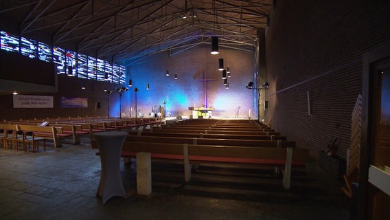 Blick in ein Kirchenschiff. Darin stehen viele Reihen Kirchenbänke, an der Wand am anderen Ende hängt ein großes Kreuz. © Screenshot 