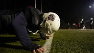 Auf einem Sportrasen macht eine Person einen Liegestütz. Sie trägt die Austrüstung der Braunschweiger Lions, inklusive dem weißen Football-Helm mit dem Emblem eines Löwens. © Screenshot 