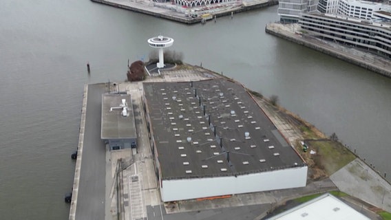 Ein Drohnenbild zeigt eine Lagerhalle auf einer Landzunge von oben. © Screenshot 