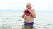 Nils Landgren steht bis zur Hüfte im Wasser und spielt auf seiner Posaune. © Screenshot 