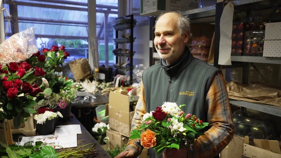 Ein Blumenhändler mit einem Strauß in der Hand in seinem Laden. © Screenshot 