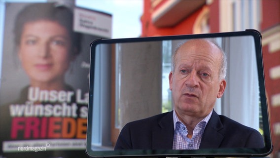 Auf einem Bildschirm zu sehen: Friedrich Straetmanns, Kandidat des Bündnis Sahra Wagenknecht. Im HIntergrund ein Plakat der Partei. © Screenshot 