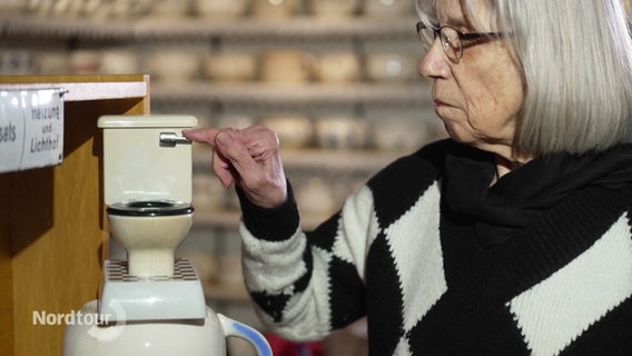 Elisabeth Hesse drückt die Spülung einer Miniatur-Toilette. © Screenshot 