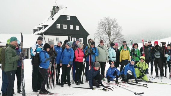 Eine Gruppe Skifahrer steht vor einer Hütte im Schnee. © Screenshot 