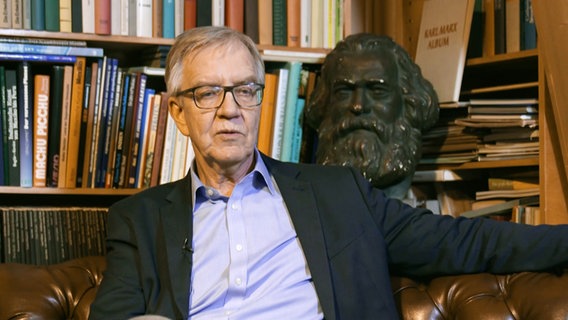 Dietmar Bartsch sitzt vor einem Bücherbord, hinter ihm eine Marx-Büste © Screenshot 