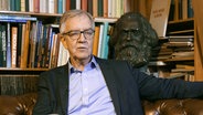 Dietmar Bartsch sitzt vor einem Bücherbord, hinter ihm eine Marx-Büste © Screenshot 