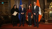 Carolina Vásquez Álvarez steht mit ihrem Mann und ihrer Tochter auf einer Bühne bei einer Einbürgerungsfeier im Hamburger Rathaus. © Screenshot 