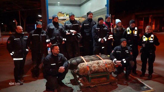 Gruppenbild: Team des Kampfmittelräumdienstes, davor zwei entschärfte Blindgänger. © Screenshot 