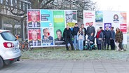 Eine Familie steht vor mehreren Wahlplakten. © Screenshot 