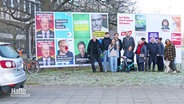 Eine Familie posiert für ein Foto vor Wahlplakaten. © Screenshot 