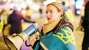 Eine junge Frau mit Megafon in der Hand ist in eine Ukraine-Flagge gehüllt. © Screenshot 