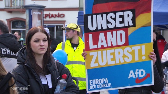 Eine junge Frau steht neben einem Wahlplakat der AfD. © Screenshot 