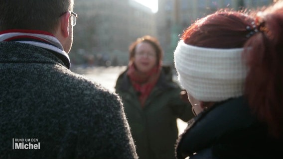 Ein Mann und eine Frau hören einer Stadtführerin bei einem Rundgang zu. © Screenshot 