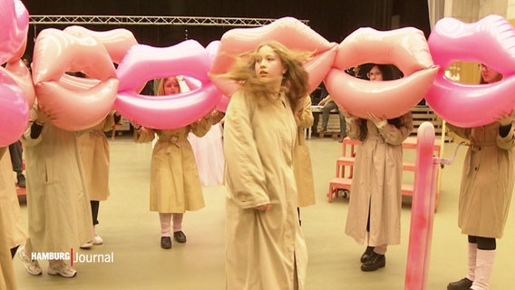 Jugendliche performen eine Theaterszene  mit langen Mänteln und Lippenförmigen Ballons. © Screenshot 