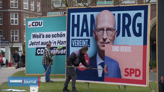 Arbeiter bringen neue Wahlplakate auf große Stellwände auf. © Screenshot 