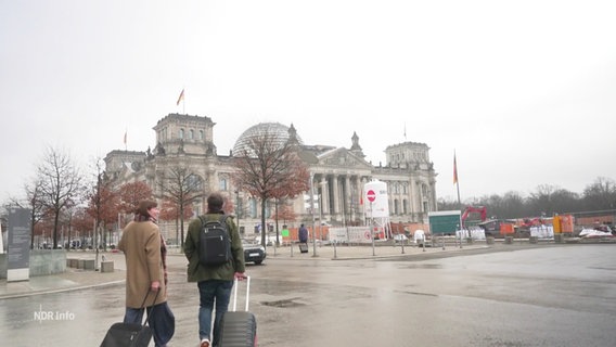 Zwei Personen mit Koffern laufen zum Bundestag. © Screenshot 