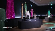 Viele glitzernde Bühnenoutfits stehen im Ausstellungsraum. © Screenshot 