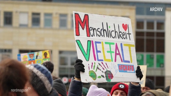 Archivfoto von einer Demonstration. Ein bubtes Schild mit der Aufschrift "Menschlichkeit Vielfalt" wird hochgehalten. © Screenshot 