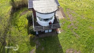 Karin Buchholz steht an der Rehling ihres Leuchtturm-Hauses und blickt in die Landschaft. © Screenshot 