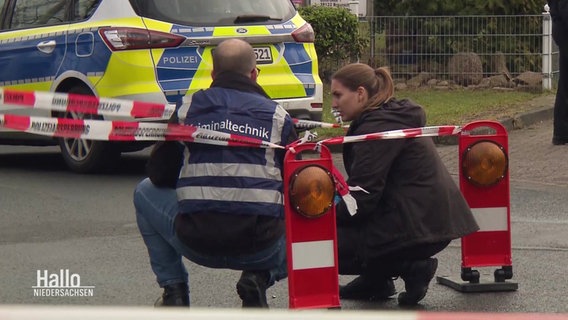 Ein Kriminaltechniker und eine Polizeibeamtin am abgesperrten Tatort. Am Boden liegt eine Patronenhülse. © Screenshot 