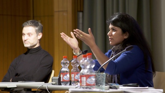 Saba-Nur Cheema und Meron Mendel sitzen bei einer Veranstaltung auf einem Podium. Saba-Nur Cheema hebt die Hände und spricht in ein Mikrofon. © Screenshot 