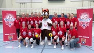 Die Volleyballerinnen stehen gemeinsam mit einem Maskottchen für ein Teamfoto zusammen. © Screenshot 