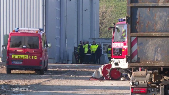 Einsatzkräfte der Feuerwehr stehen auf dem Gelände einer Mülldeponie. © Screenshot 