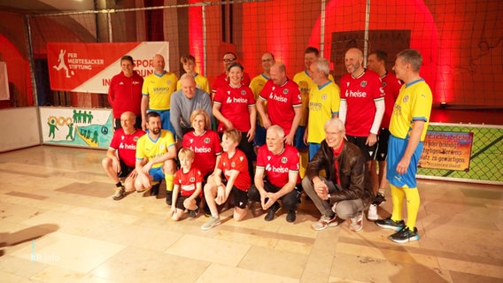 Mehrere Spieler in rot gelben Trikots stehen auf einem in einer Kirche aufgebauten Fußballfeld. © Screenshot 