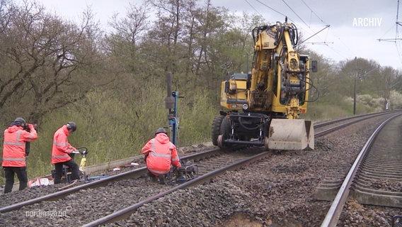 Arbeitende bei einer Baustelle an Bahngleisen, daneben ein Bagger auf Schienen. © Screenshot 