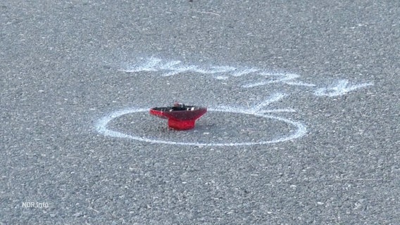 Ein abgefallenes Fahrradrücklicht liegt in der Mitte einer kreisrunden Unfall-Markierung auf dem Straßenasphalt. © Screenshot 