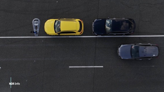 Blick aus der Vogelperspektive auf eine simulierte Verkehrssituation auf einer Auto-Test-Anlage: Ein Auto fährt an einer Reihe parkender Autos vorbei, an dessen Ende sich ein Kind auf die Straße begibt. © Screenshot 