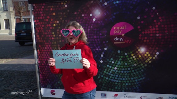 Eine Frau mit Herzsonnenbrille und einem Schild mit der Aufschrift "Gerechtigkeit Jetzt!" auf dem equal pay day in Boizenburg. © Screenshot 