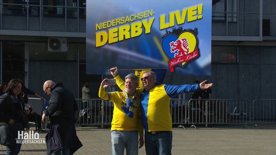 Zwei männliche Fans machen ein Selfie vor einem Plakat. © Screenshot 