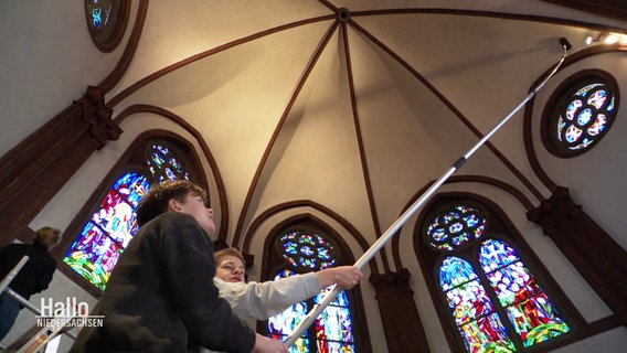 Zwei Jungs putzen mit einem langen Staubwedel die Kirchendecke. © Screenshot 