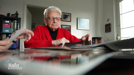 Josef Slominski sitzt am Tisch vor vielen Fotos. © Screenshot 