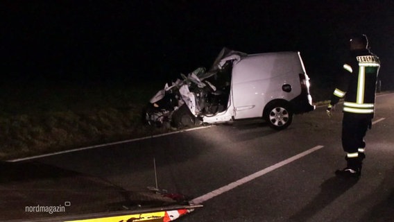 Ein zerstörter Wagen steht am Straßenrand, ein Polizist steht daneben. © Screenshot 