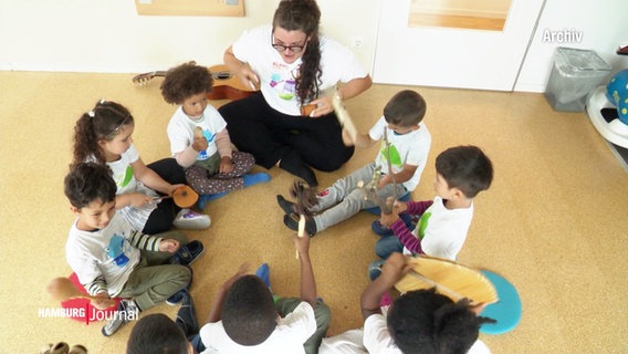 Kinder sitzen in einem Kreis und spielen mit Musikinstrumenten. © Screenshot 