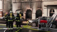 Feuerwehrleute stehen vor einem ausgebrannten Gebäude. © Screenshot 