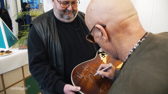 City-Legende Toni Krahl unterschreibt auf seiner versteigerten Gitarre. © Screenshot 