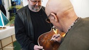 City-Legende Toni Krahl unterschreibt auf seiner versteigerten Gitarre. © Screenshot 