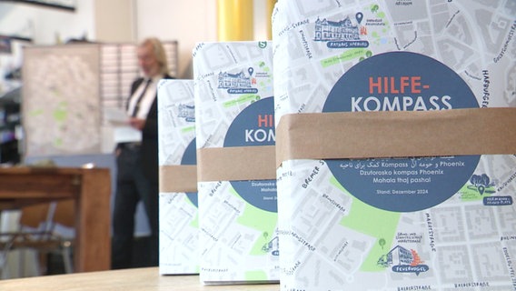 Flyer zum neuen Hilfs-Kompass für das Harburger Phoenix-Viertel stehen auf einem Tisch. © Screenshot 