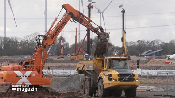 Auf einer Baustelle schaufelt ein Bagger Erde auf einen LKW. © Screenshot 