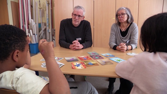 Elisabeth Rickert und Thomas Hoffmann im Gespräch mit zwei Kindern. © Screenshot 