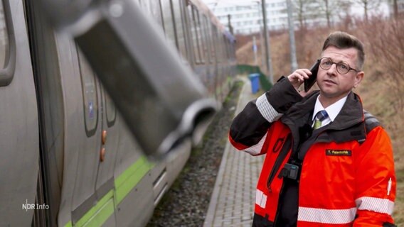 ÜSTRA-Mitarbeiter steht neben einer Straßenbahn und telefoniert. © Screenshot 