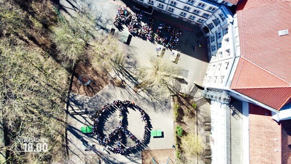 Schüler bilden gemeinsam ein Peace-Zeichen und auch das Wort Peace auf einem Schulhof. © Screenshot 