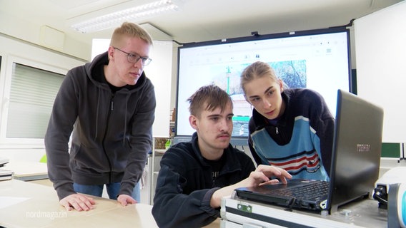 Drei Jugendliche sitzen an einem Laptop in einem Klassenzimmer. © Screenshot 