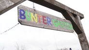 Von einem Holzgerüst hängt ein Schild mit der Aufschrift "Bunter Garten". © Screenshot 