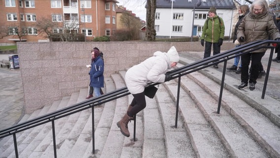 Eine ältere Dame rutscht bäuchlings einen Handlauf hinab. © Screenshot 