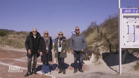 Vier Personen stehen vor einem Eingang zwischen Dünen zu einem Strand. © Screenshot 