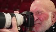 Fotograf Geert Maciejewski kneift sein Auge beim Blick durch eine Fotokamera zu. © Screenshot 